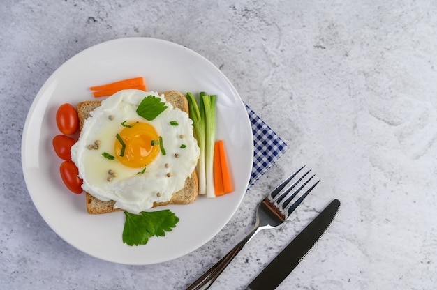 A fried egg laying on a toast, topped with pepper seeds with carrots and spring onions.