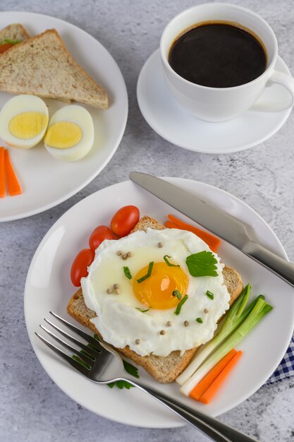 A fried egg laying on a toast, topped with pepper seeds with carrots and spring onions.