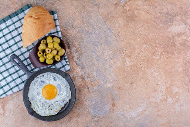 Fried egg in a pan with green olives and bread