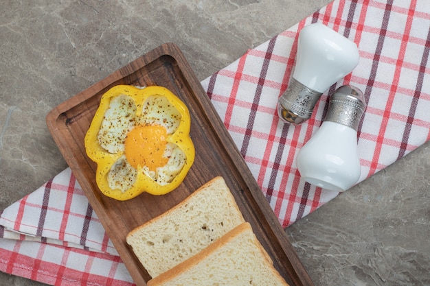 Fried egg in pepper and bread slices on wooden plate. High quality photo