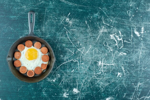 Жареное яйцо и нарезанные сосиски на металлической сковороде. Фото высокого качества
