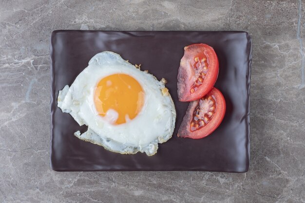 Fried egg and tomato slices on dark plate.