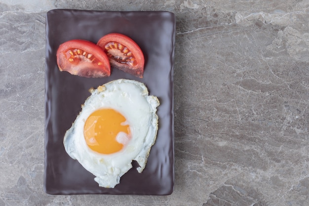 Free photo fried egg and tomato slices on dark plate.