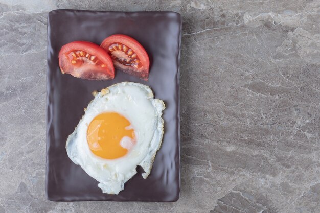 Жареные яйца и ломтики помидоров на темной тарелке.