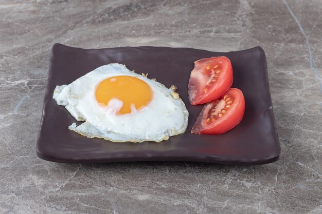 Fried egg and tomato slices on dark plate. 