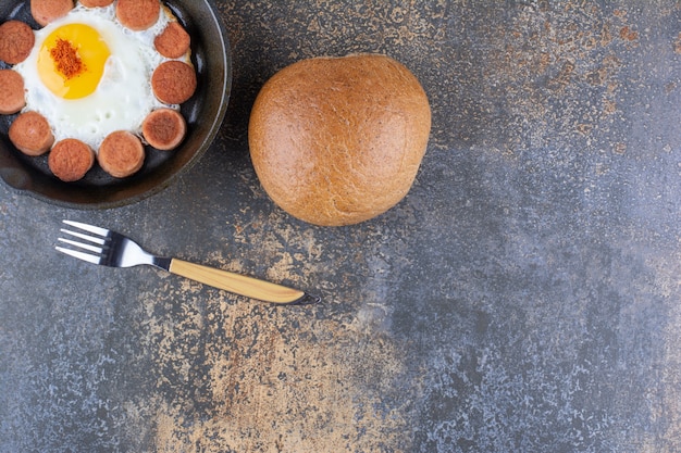 Fried egg with sausages in a pan served with a bread bun