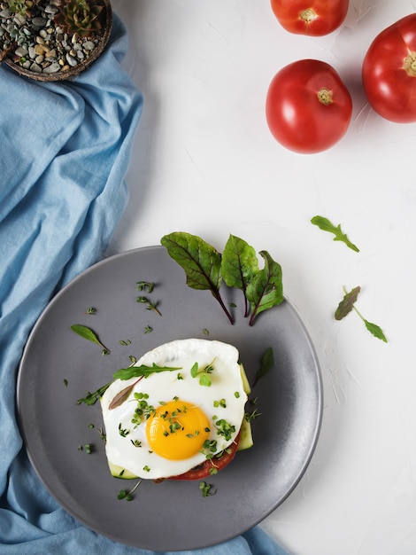 Fried egg with tomatoes and leaves of arugula and thyme on bread in a gray plate