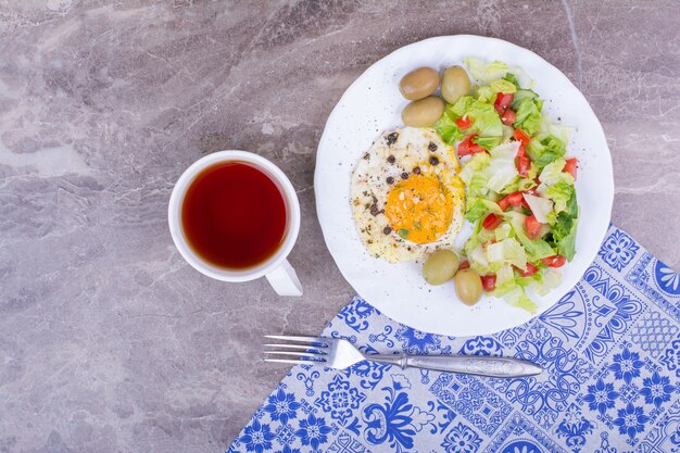 Fried egg with vegetable salad and a cup of tea.