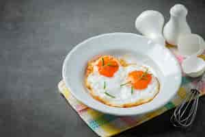 Бесплатное фото Жареные яйца в белой тарелке на темной поверхности