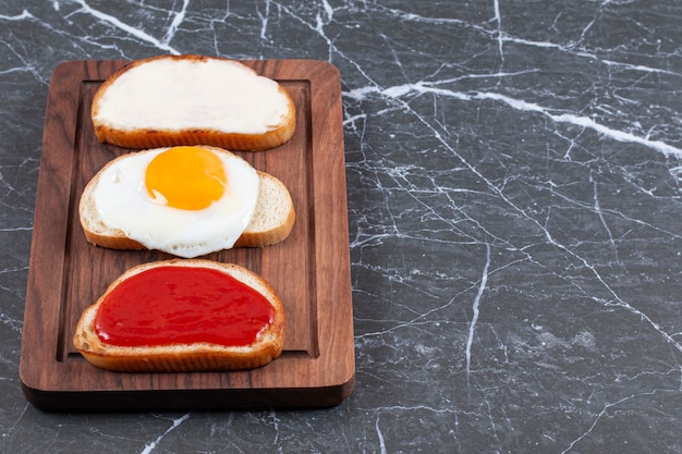 Fried eggs, jam and cheese on individually sliced bread on the board , on the marble surface