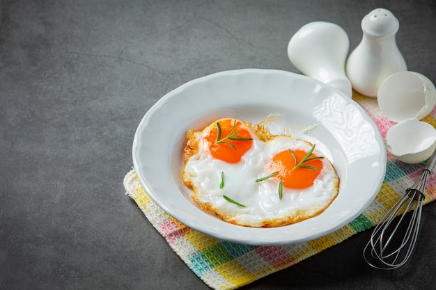 Fried eggs in a white plate on dark surface