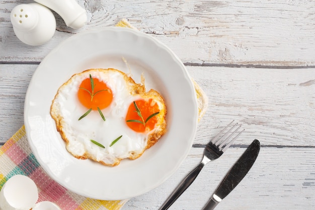 Fried eggs in a white plate on white wooden surface