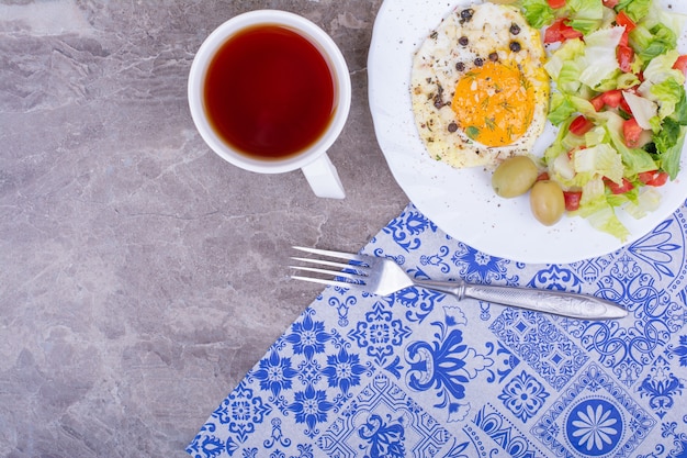 Free photo fried eggs with green salad and a cup of tea.