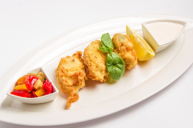 Fried fish in batter with sauce, lemon and vegetables