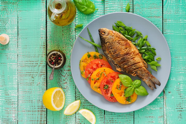 Fried fish carp and fresh vegetable salad on wooden table. Flat lay. Top view