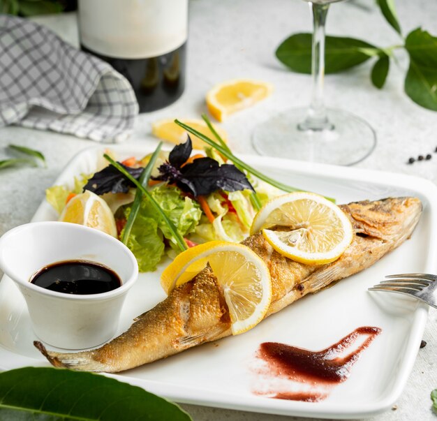 Жареная рыба, украшенная дольками лимона, подается с салатом и нар-шарабом