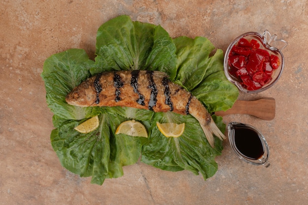 Fried fish on lettuce with lemon slices, pickles and pomegranate sauce.