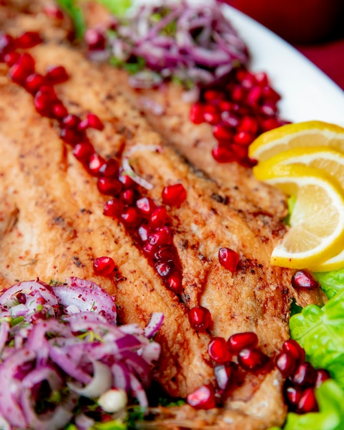 fried fish served with pomegranate lettuce onion and lemon slices