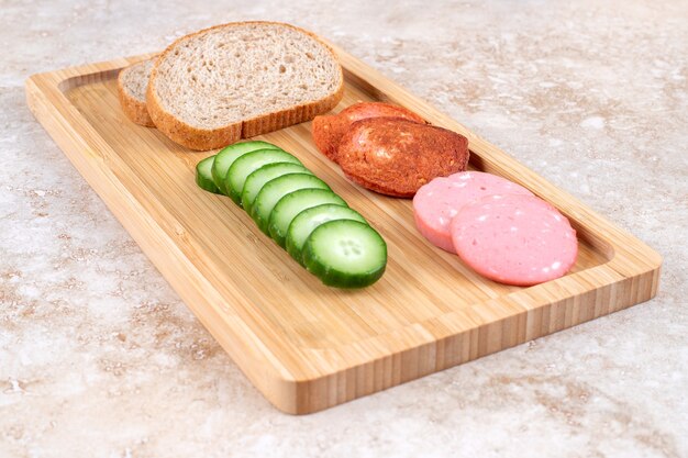 Fried and fresh salami slices on wooden board with bread and cucumber.