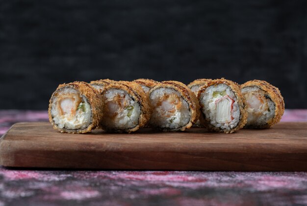 Fried hot sushi rolls on a wooden board .