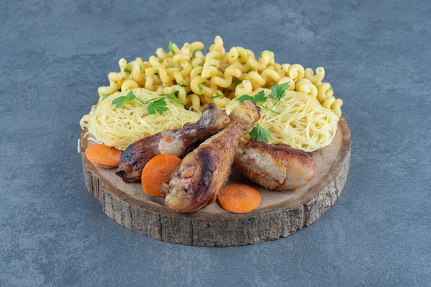 Fried legs, macaroni and spaghetti on wood piece. 