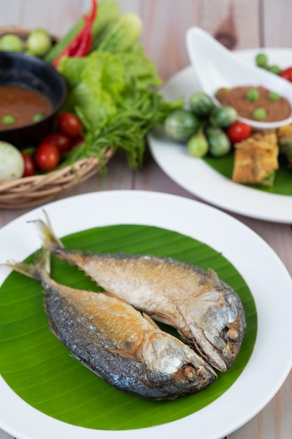 Fried mackerel placed on a white plate on a wooden floor