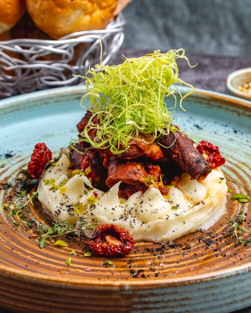 Fried meat placed on mashed potato garnished with shredded bell pepper and thyme