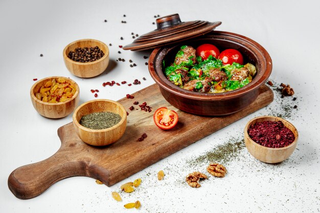 Fried meat with greens and tomatoes in a clay pot