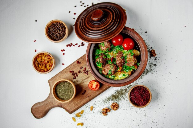 Fried meat with greens and tomatoes in a clay pot