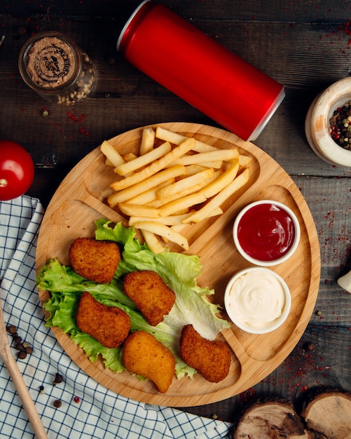 Fried nuggets with french fries on wooden board