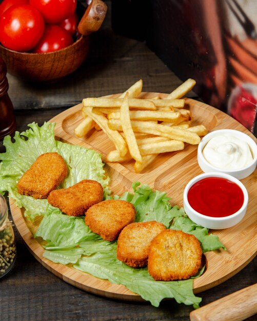 Fried nuggets with french fries on wooden board