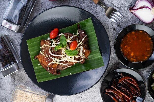 Fried pork topped with sesame seeds put on a banana leaf in a black dish.