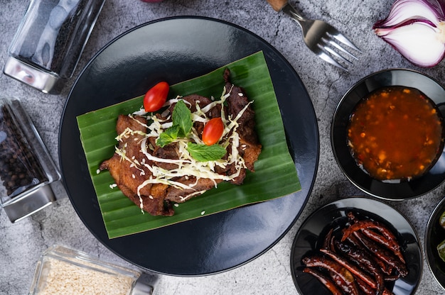 Fried pork topped with sesame seeds put on a banana leaf in a black dish.