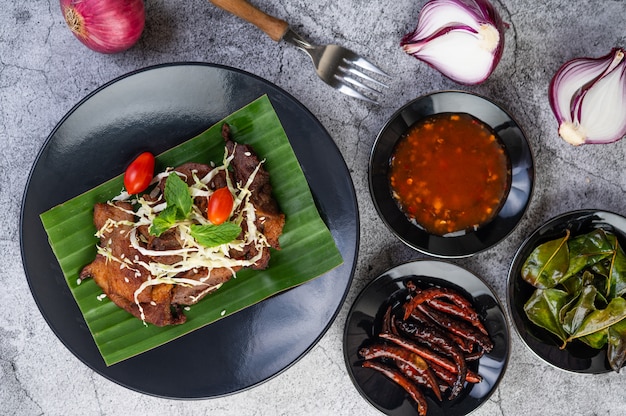 Fried pork topped with sesame seeds put on a banana leaf in a black dish.