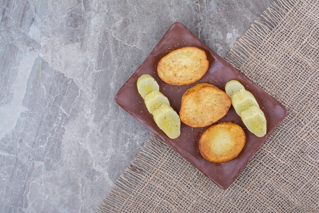 Жареные кусочки картофеля и маринованные огурцы на тарелке.