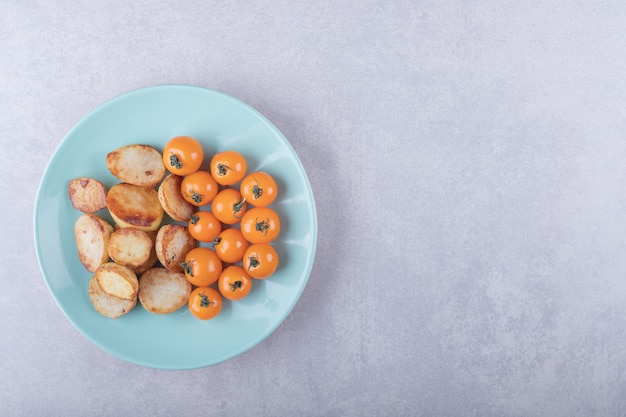 Жареный картофель и помидоры черри на синей тарелке.