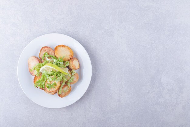 Fried potatoes decorated with lemon and lettuce on white plate. 