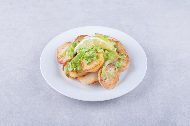 Fried potatoes garnished with lemon on white plate.