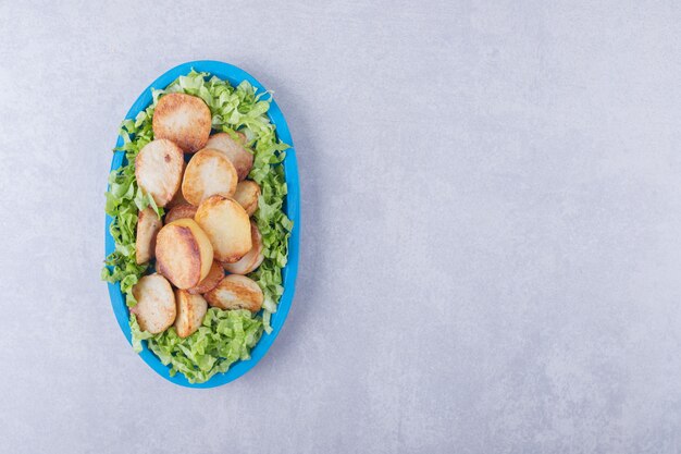 Fried potatoes and lettuce on blue plate. 