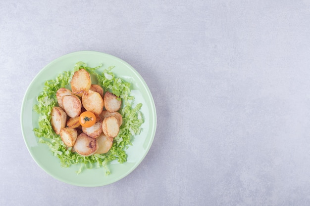 Fried potatoes and lettuce on green plate. 