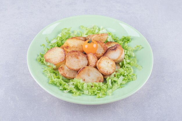 Fried potatoes and lettuce on green plate. 