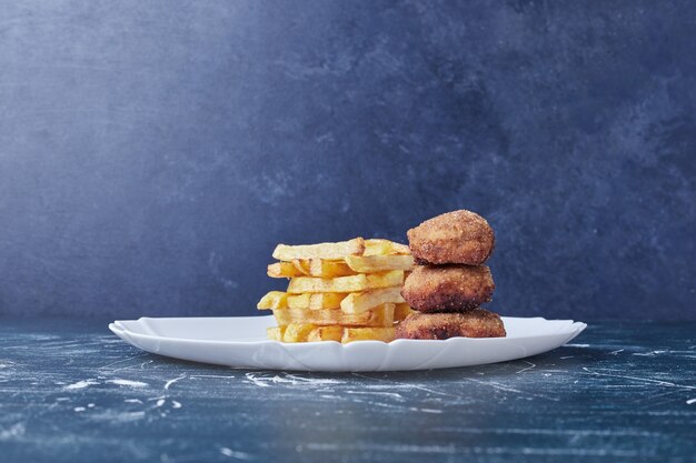 Fried potatoes and nuggets in a white plate.