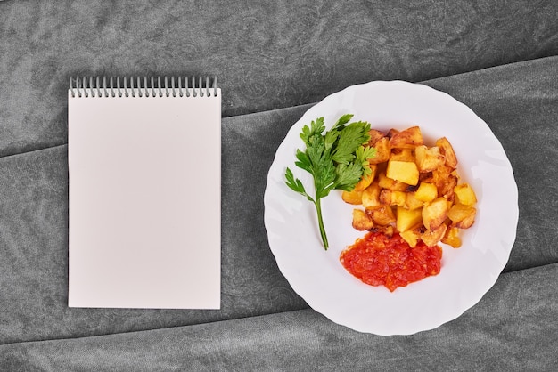 Foto gratuita patate fritte in salsa di pomodoro con un ricettario.