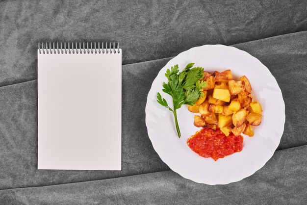 Fried potatoes in tomato sauce with a recipe book.