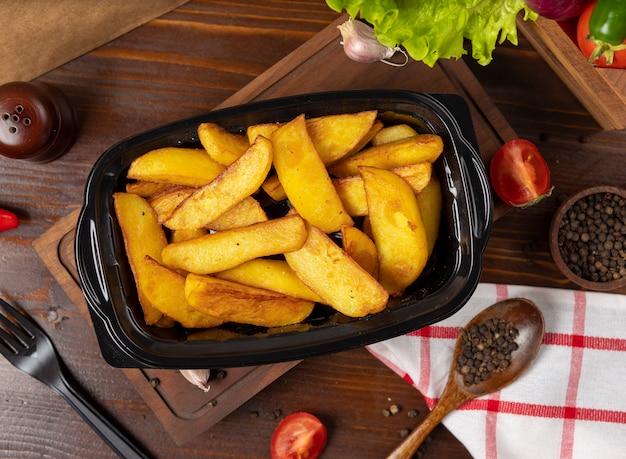 Fried potatoes with herbs takeaway in black container.