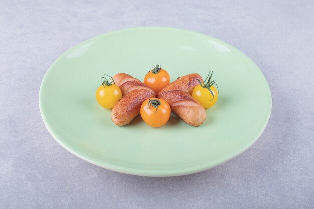 Fried sausages and cherry tomatoes on green plate. 