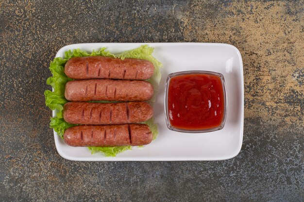 Fried sausages and ketchup on white plate with lettuce.