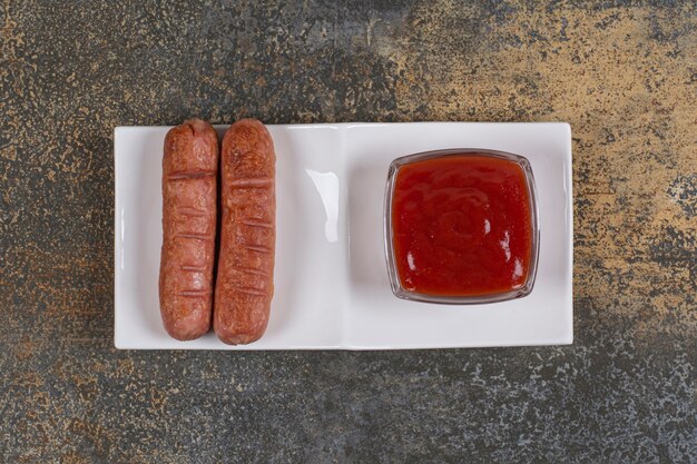 Жареные сосиски и кетчуп на белой тарелке.