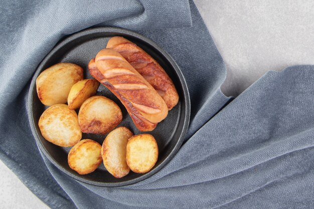 Fried sausages and potatoes on black plate.