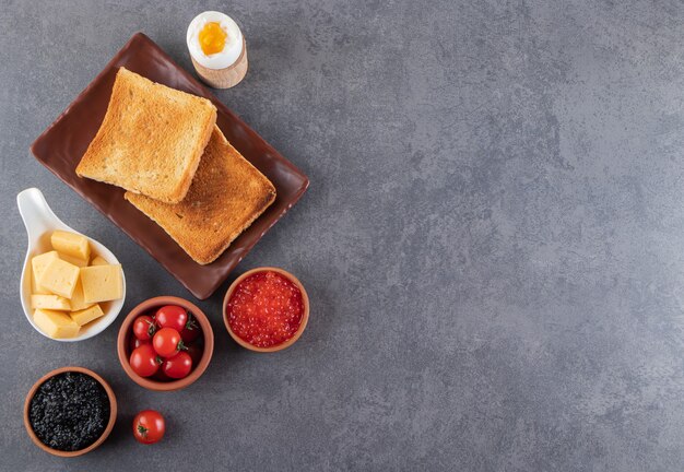 Fried sliced bread with red cherry tomatoes and boiled egg placed on stone background.